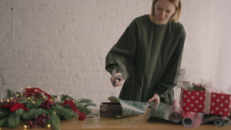 portrait a young woman decorating a gift on a wooden table with garlands turns over and puts on the table a ready-made christmas box crushed with a ribbon