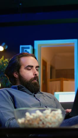 vertical video man working on laptop at home with tv show playing in background