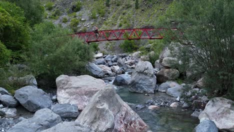 a mountain river flowing over rocky terrain in theth, albania, aerial dolly up stream as person walks across thethi bridge