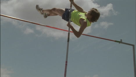 a young man executes a pole vault and lands on a mat