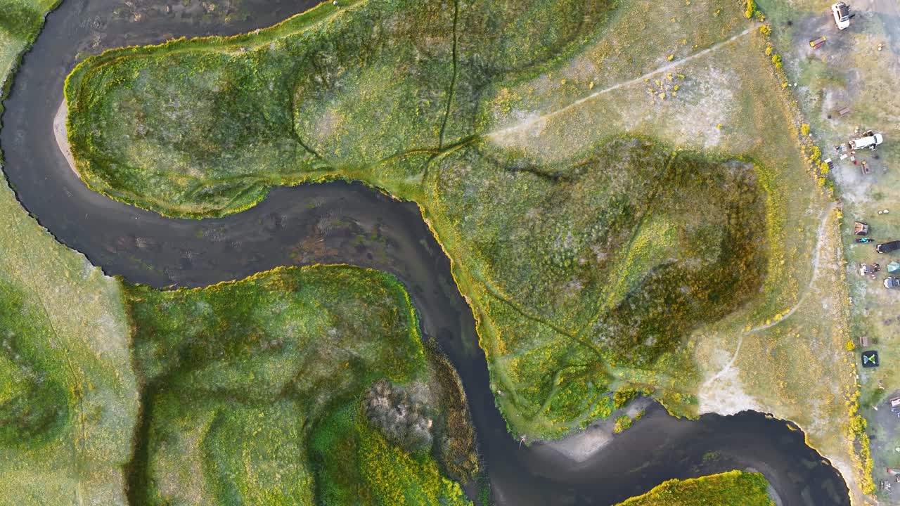 Top down drone shot following a meandering alpine river through green meadow near the Mammoth Lakes Basin in bright summer light. Clear water channels marsh textures create a graphic abstract plate