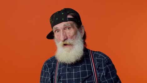 Happy-playful-elderly-bearded-man-in-sunglasses-and-cap-blinking-eye,-looking-at-camera-with-smile