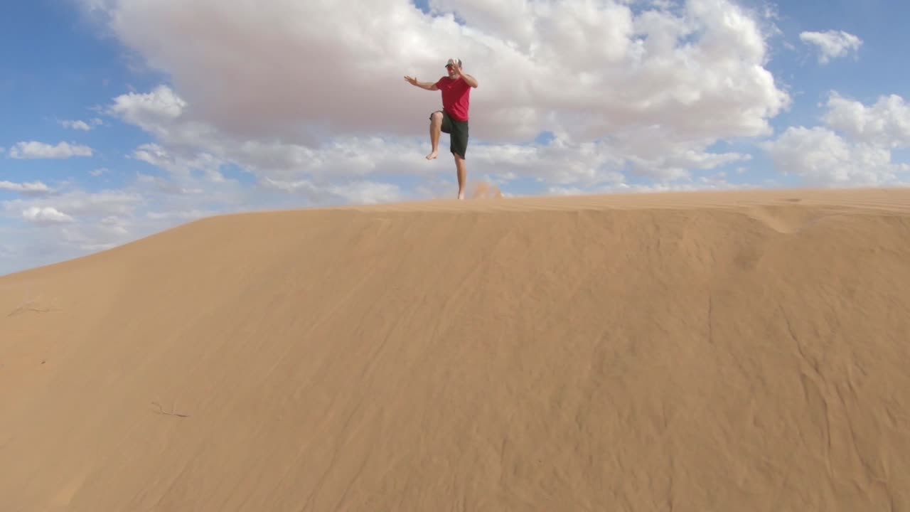Un uomo che corre e salta sopra una grande duna di sabbia dorata.