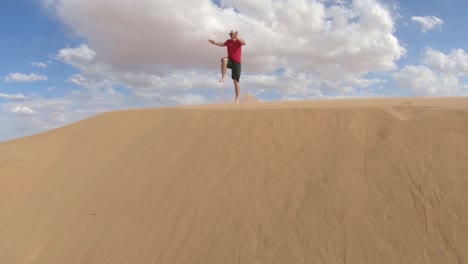 a man running a jumping over a large golden sand dune.