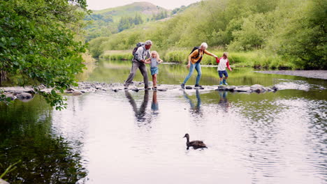 Zeitlupenaufnahme-Von-Großeltern,-Die-Ihren-Enkeln-Beim-Wandern-Im-Britischen-Seengebiet-Helfen,-Den-Fluss-Zu-überqueren