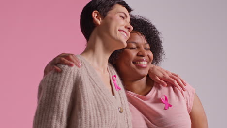 Studio-Portrait-Of-Two-Women-Wearing-Pink-Breast-Cancer-Awareness-Ribbons-Hugging-Against-Pink-Background-1