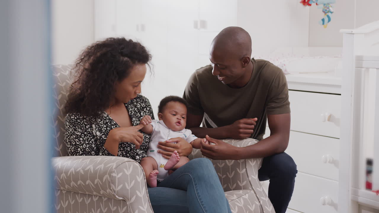 Loving Parents Sitting In Chair Cuddling Baby Son In Nursery At Home