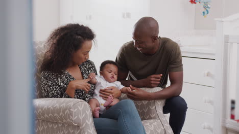 loving parents sitting in chair cuddling baby son in nursery at home