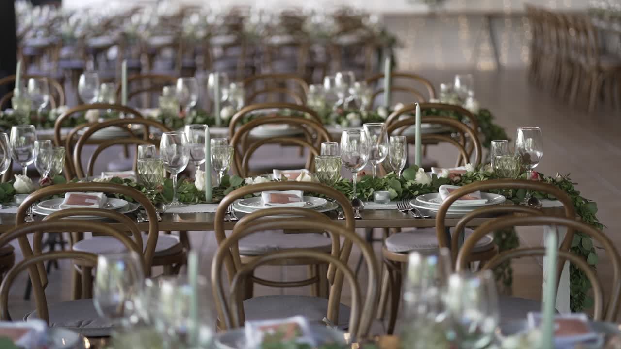 Elegante allestimento per ricevimento di matrimonio con sedie in legno, bicchieri e centrotavola di verde.