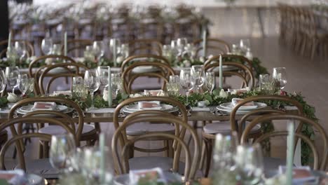 elegant wedding reception setup with wooden chairs, glassware, and greenery centerpieces