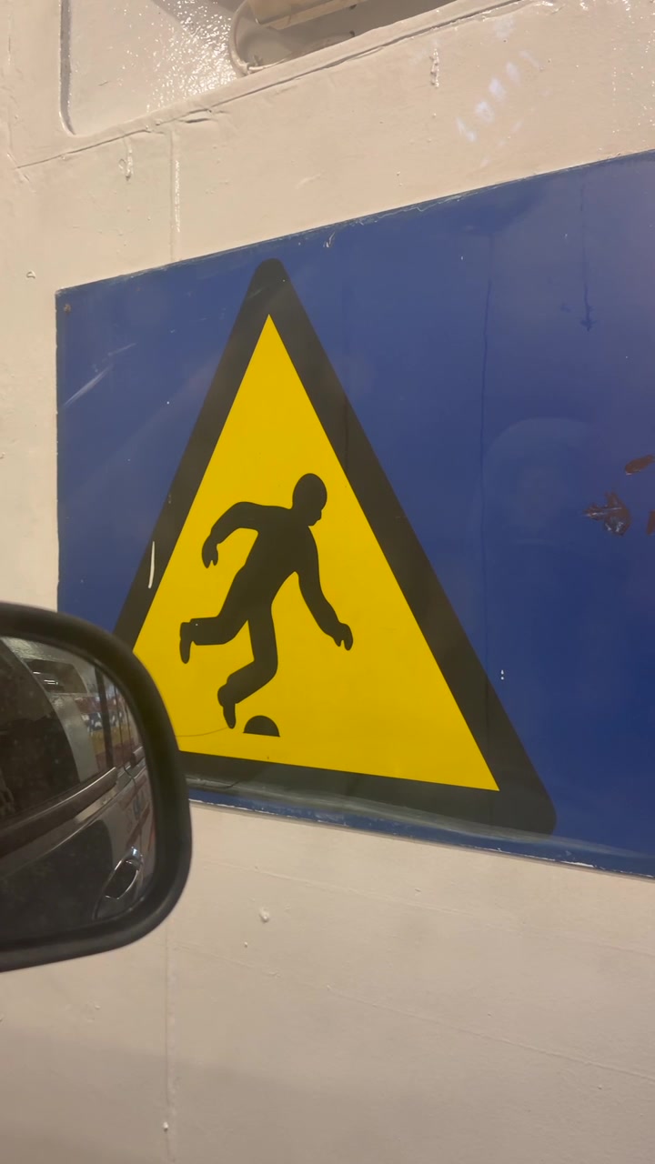 Yellow triangular warning sign showing slipping hazard on wet surface viewed from inside a car in enclosed space