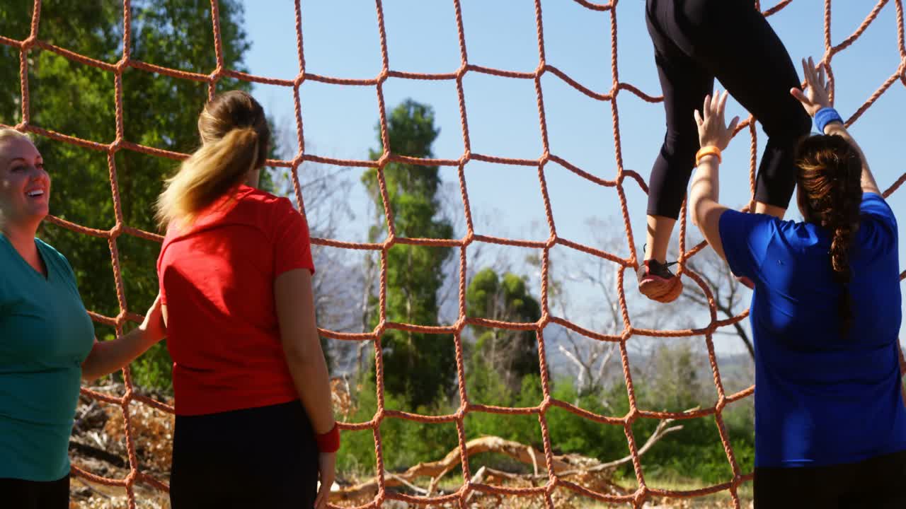 장애물 코스 중 등반 네트워크에서 여성을 돕는 여성 트레이너