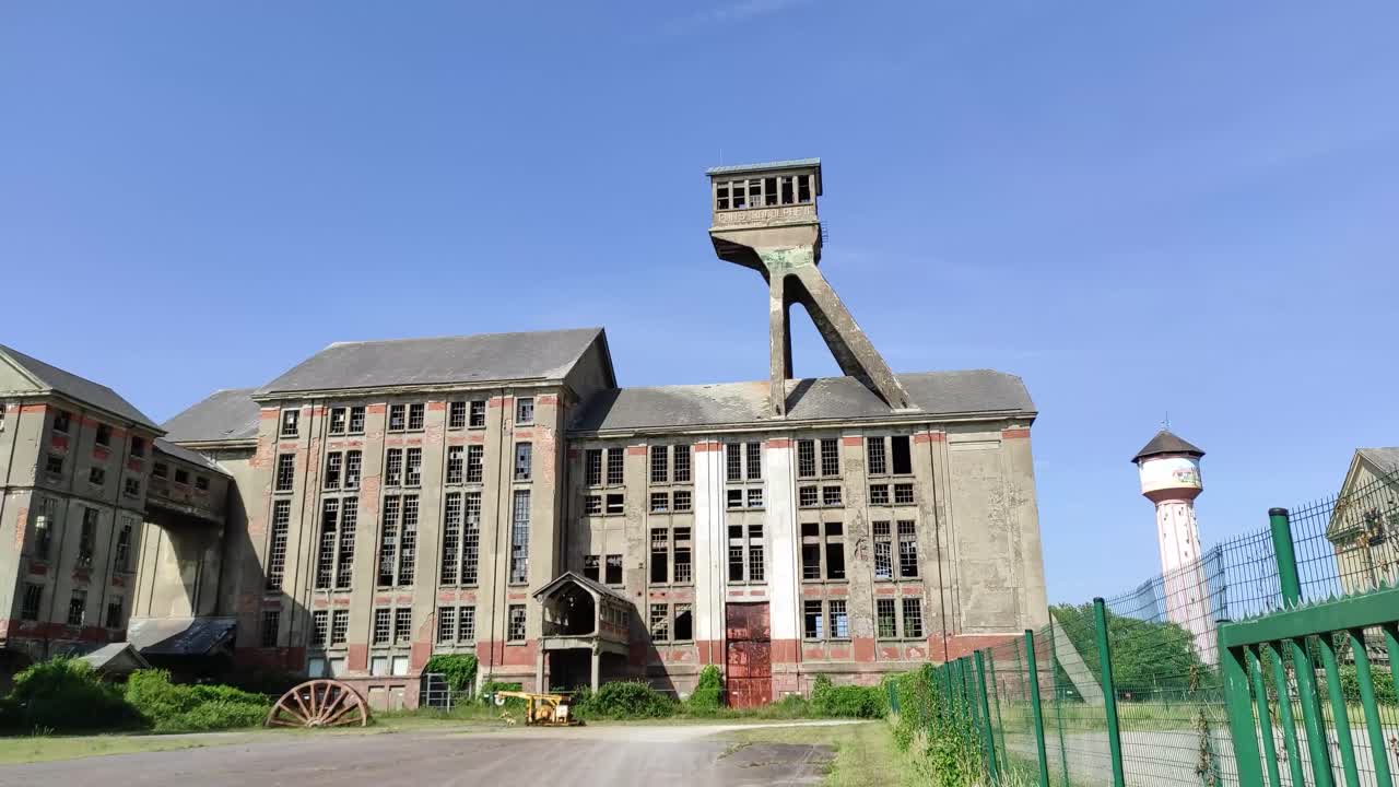 Old buildings of a colliery serving as open-air museum with broken windows and a conveyor tower, panning shot