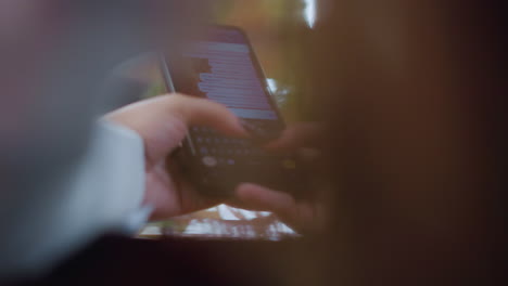 close-up of black cell phone being used for chatting on a wooden table, fingers typing on keyboard, screen displaying text messages, blurred light effects around creating soft and warm ambiance