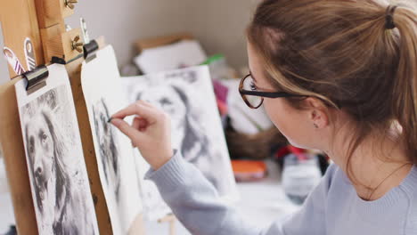 Female-Teenage-Artist-Sitting-At-Easel-Drawing-Picture-Of-Dog-From-Photograph-In-Charcoal