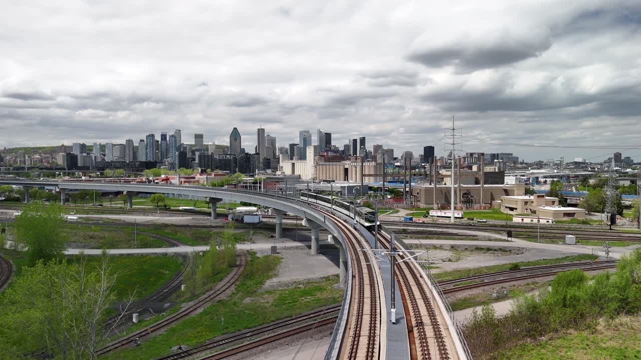 Aerial shot of downtown Montreal skyline under overcast sky, features REM train moving towards downtown area urban setting.