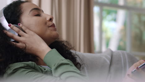 happy teenage girl listening to music wearing headphones relaxing on sofa at home texting with smartphone enjoying sharing lifestyle on social media