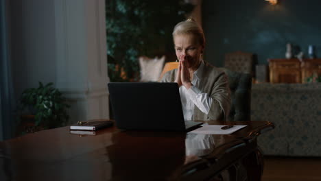 excited senior woman receiving good news on laptop computer in luxury room