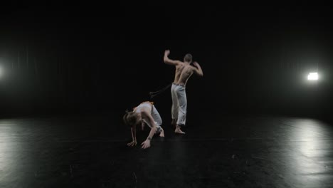 group of a professional dancers are practicing capoeira in darkness against a spotlight on a black background of studio. afro-brazilian martial art that combine elements of dance.