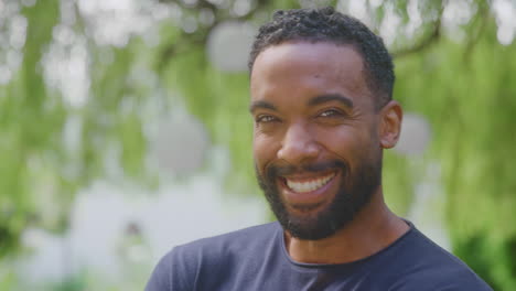 head and shoulders portrait of relaxed smiling man standing in garden at home after retirement