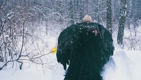 tired actress in black dress with wings walks through snow