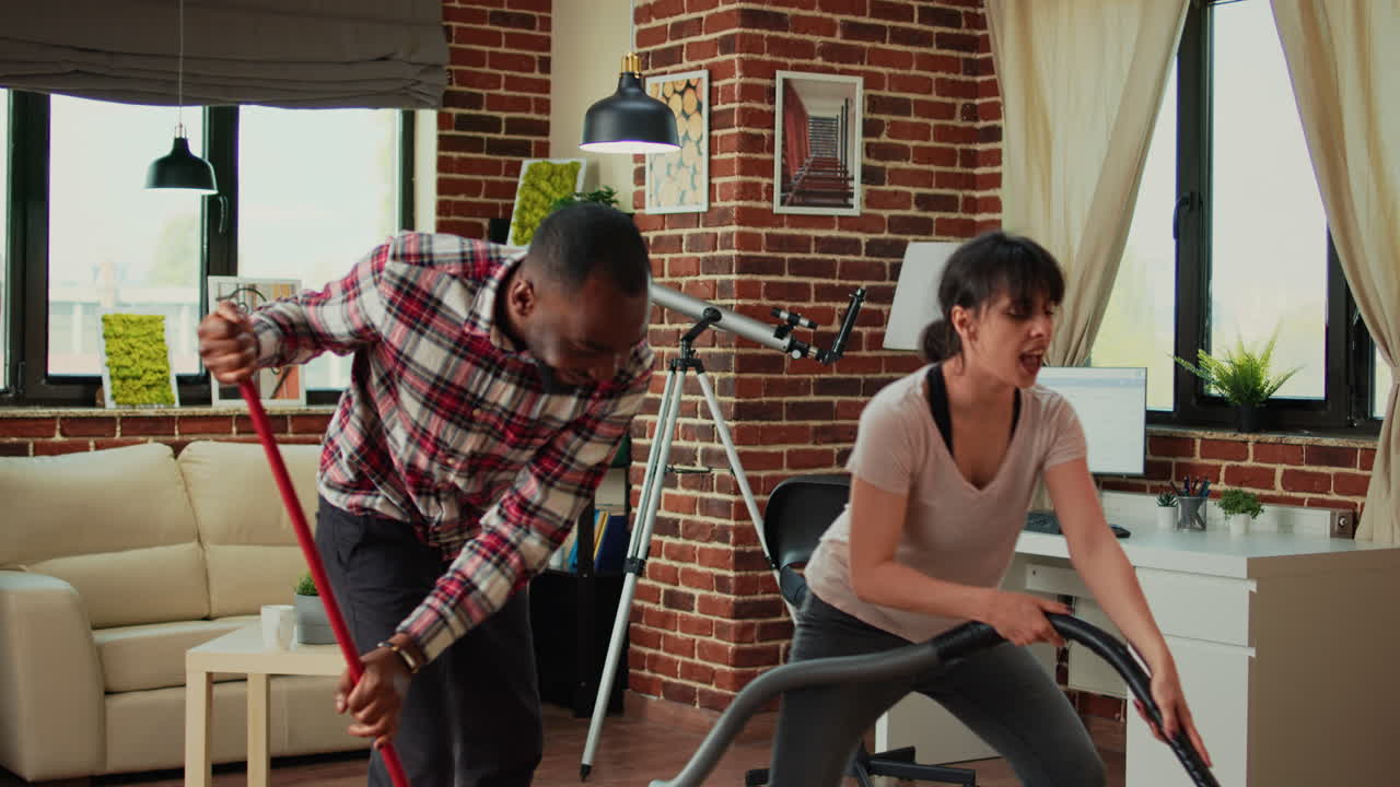 Diverse couple showing dance moves and having fun cleaning apartment
