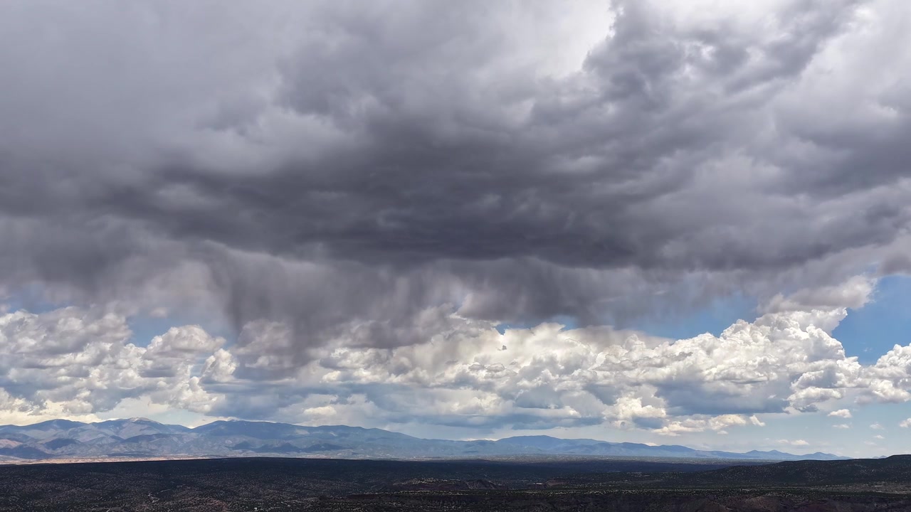 4K drone-timelapse fanger en nær forgrundsregnbyge fra en mørk stormsky. Filmisk luftbevægelse afslører tunge, hvirvlende skyer, der forvandler sig over en barsk bjergkæde i baggrunden.