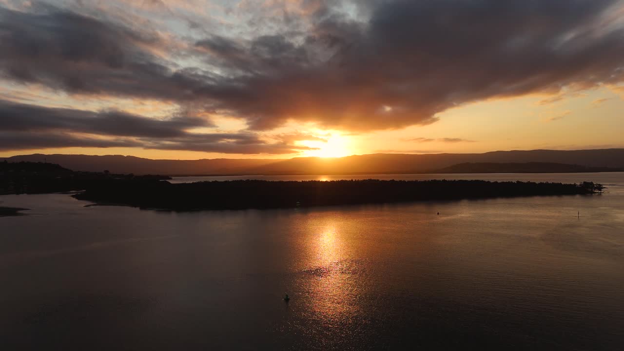 Serene Lake Illawarra at golden hour with calm waters reflecting the vibrant colors of the sunset, aerial dolly with reflection of orange beam