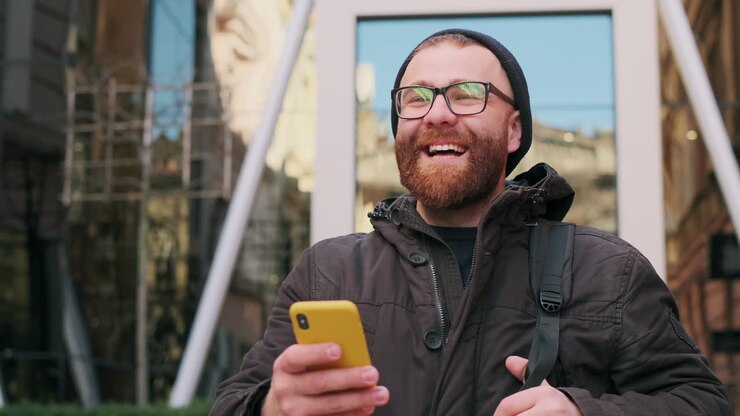 Happy bearded man laughing while using smartphone outdoors