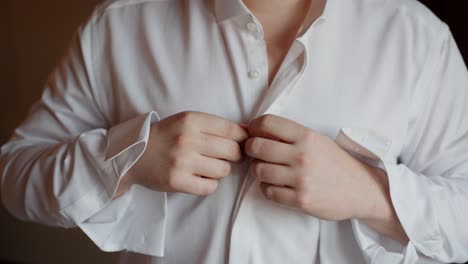 dressing in a white shirt, focusing on buttoning up for a wedding preparation scene