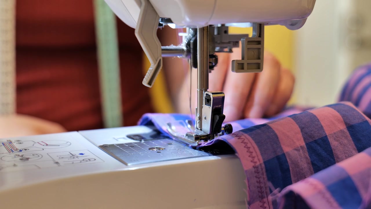 Precision tailoring work showing hands guiding checkered fabric through a sewing machine.