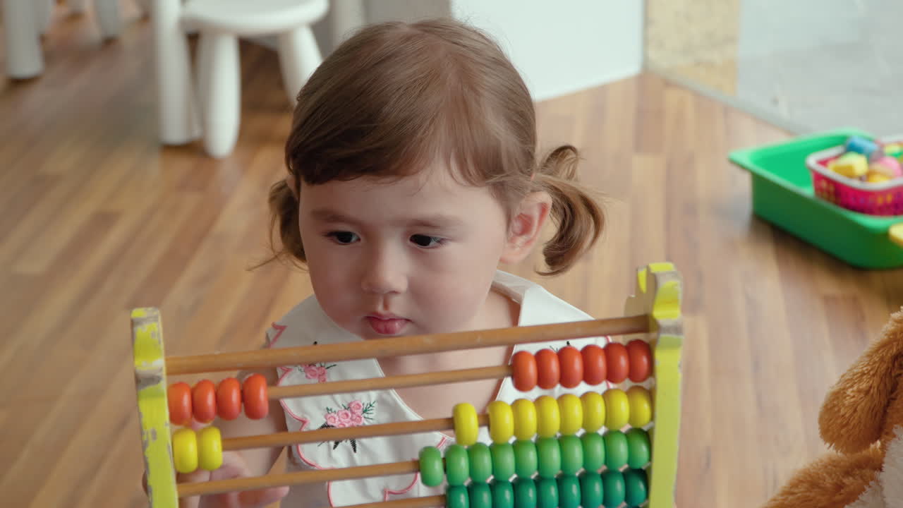 adorable niña concentrada jugando con ábaco colorido en la sala de juegos interior