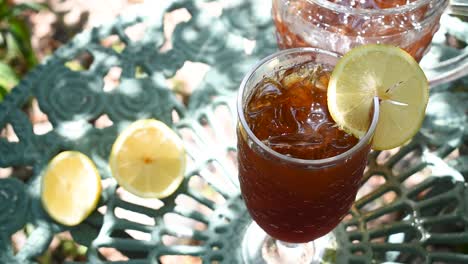 tall glass of ice tea with lemon in outdoor summer garden wind blowing leaves shadows