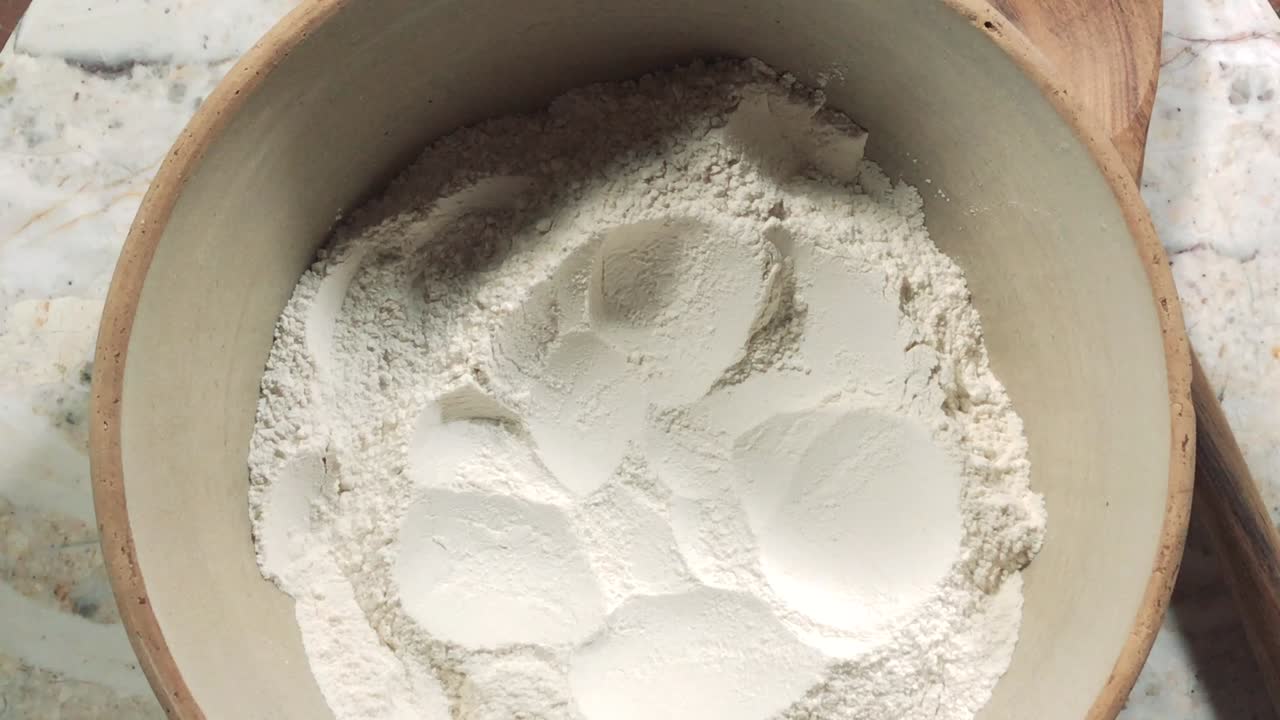 overhead view of cracking eggs into flour