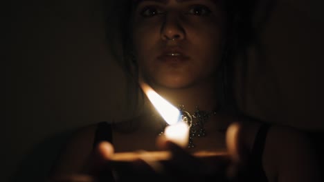 a woman in the dark house with a lit candle in her hands moving the candle looking into the camera