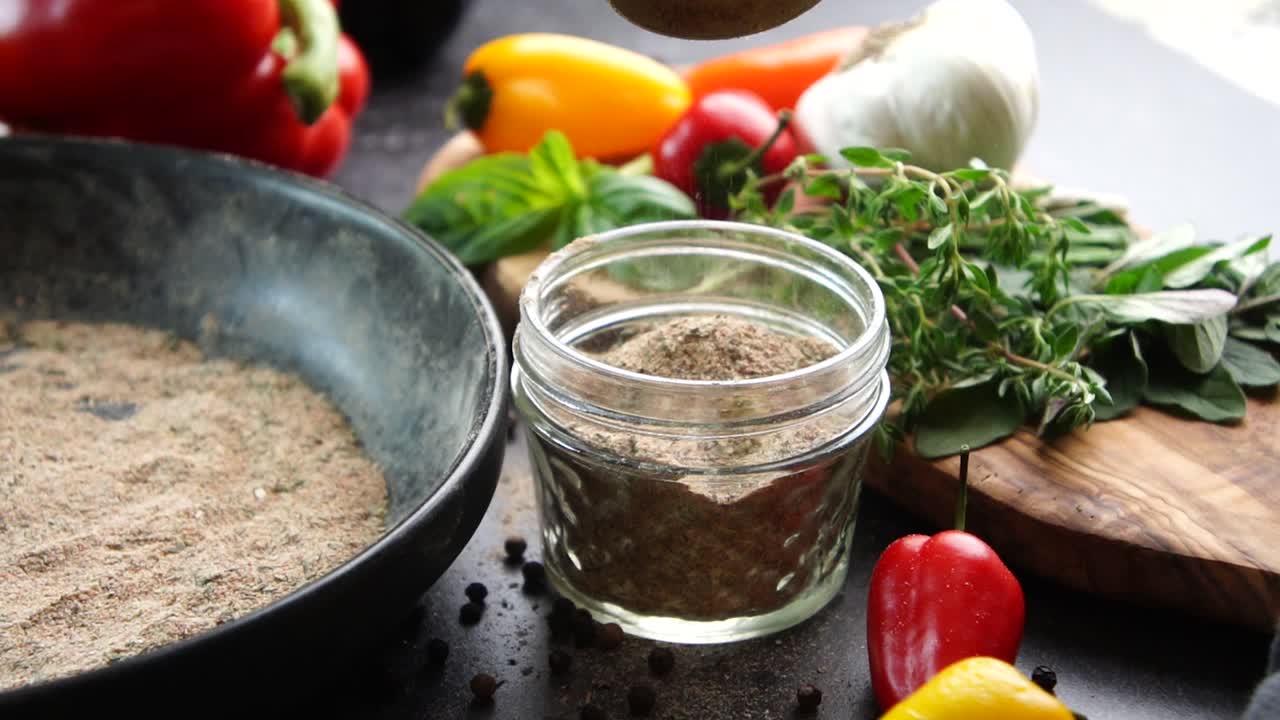 Making a vibrant Cajun Spice Blend, mixing red paprika, cayenne pepper, oregano, thyme, white garlic onion powder and black pepper in a bowl, creating a striking contrast against a black background.