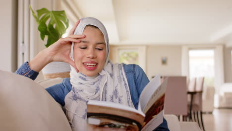 Happy-biracial-woman-in-hijab-reading-book-on-sofa-at-home-with-copy-space,-slow-motion