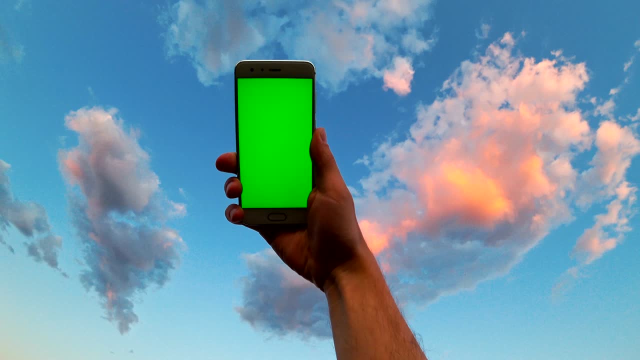la mano del hombre sostiene un teléfono móvil con pantalla verde en el fondo del cielo nublado y gira