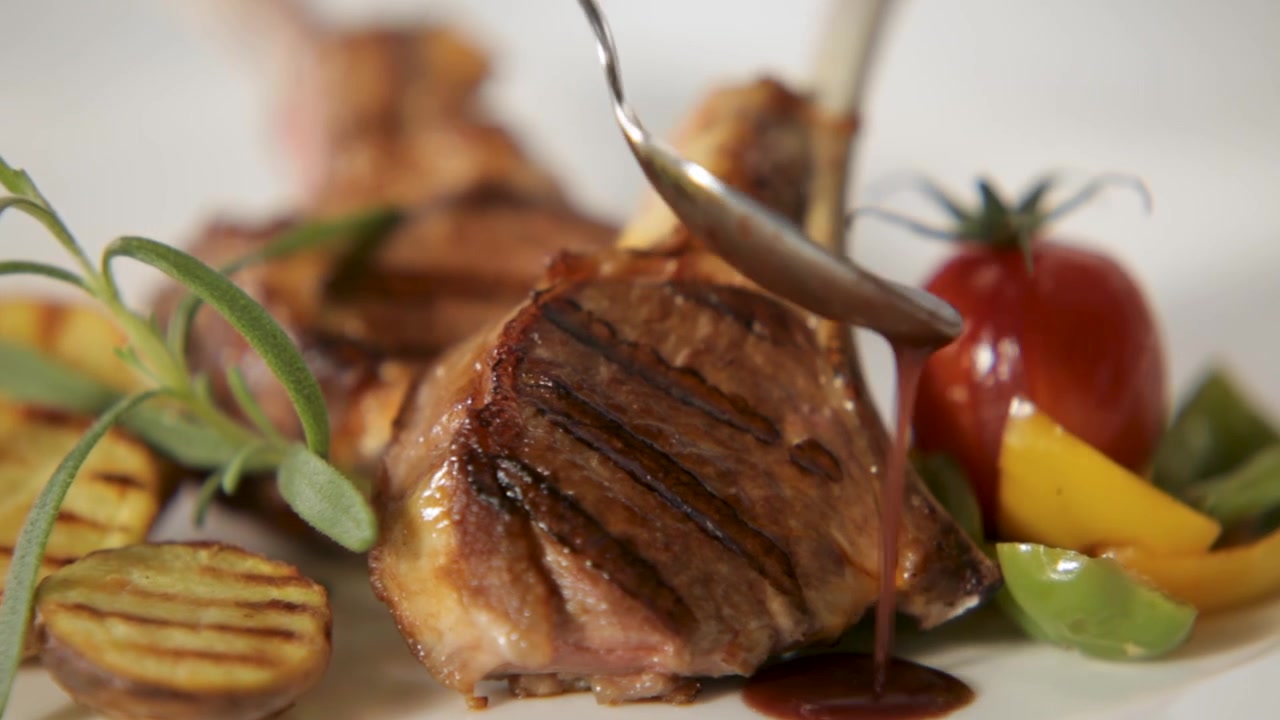 Costolette d'agnello succulente al rosmarino, verdure grigliate e una ricca salsa versata sopra.