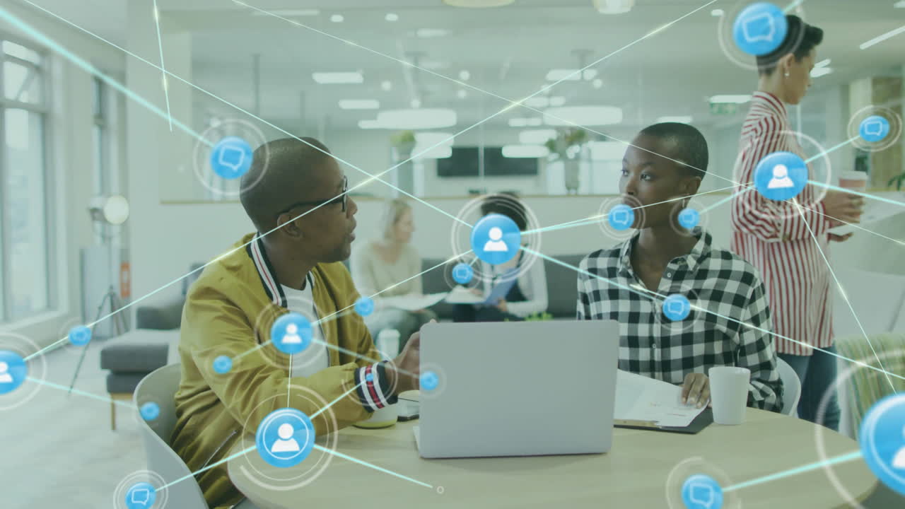 Animation of network of connections with icons over diverse colleagues using laptop in office