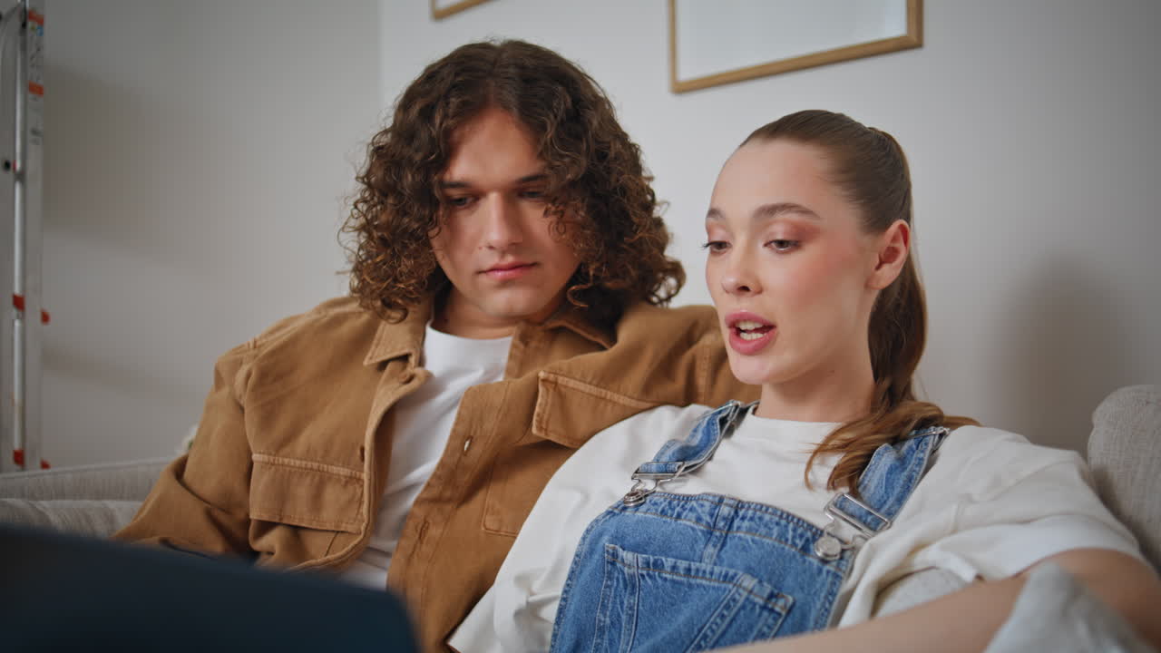 Young couple looking laptop sitting home couch having conversation closeup