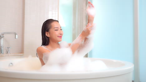 a beautiful young woman in a bubble bath washes her arms and shoulders