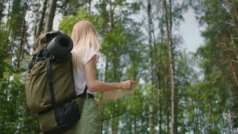 slow motion of a young tourist woman with a road card and a compass in the woods searching for the footpath.