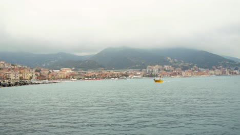 small yellow boat sails in the bay of the port of varazze on a cloudy day,background varazze town , liguria italy