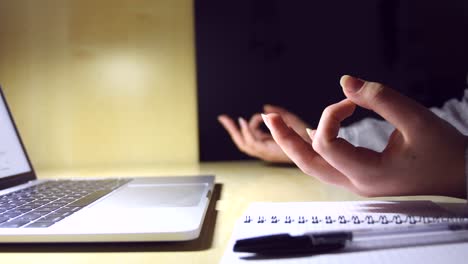 young female hands doing yoga on a minimal office workplace with a laptop, a notebook and a pen, for stress relief during work