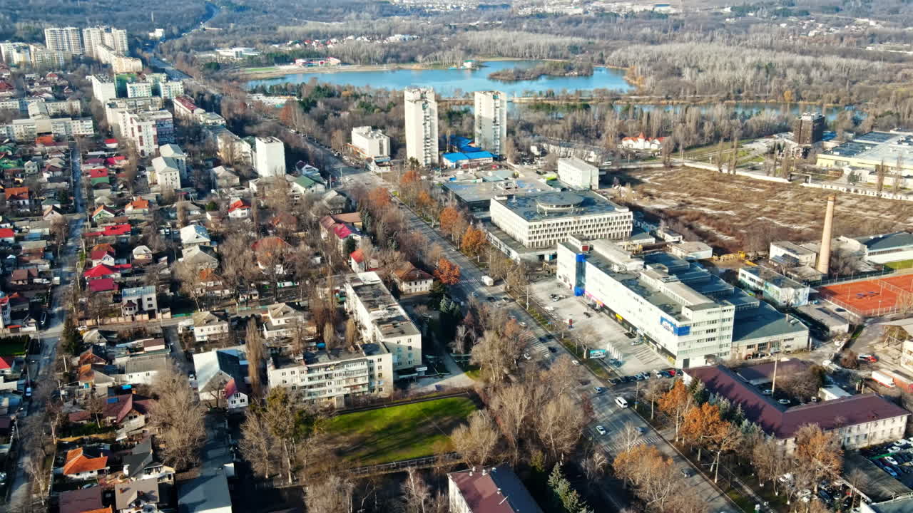 Aerial drone view of Chisinau. Panorama view of multiple buildings, road with moving cars, bare trees, lake and hills in the distance. Good weather. Moldova