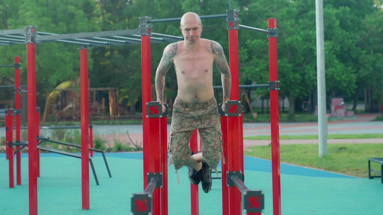 Bald Man with Tattoos Doing Dips on Parallel Bars at Outdoor Gym