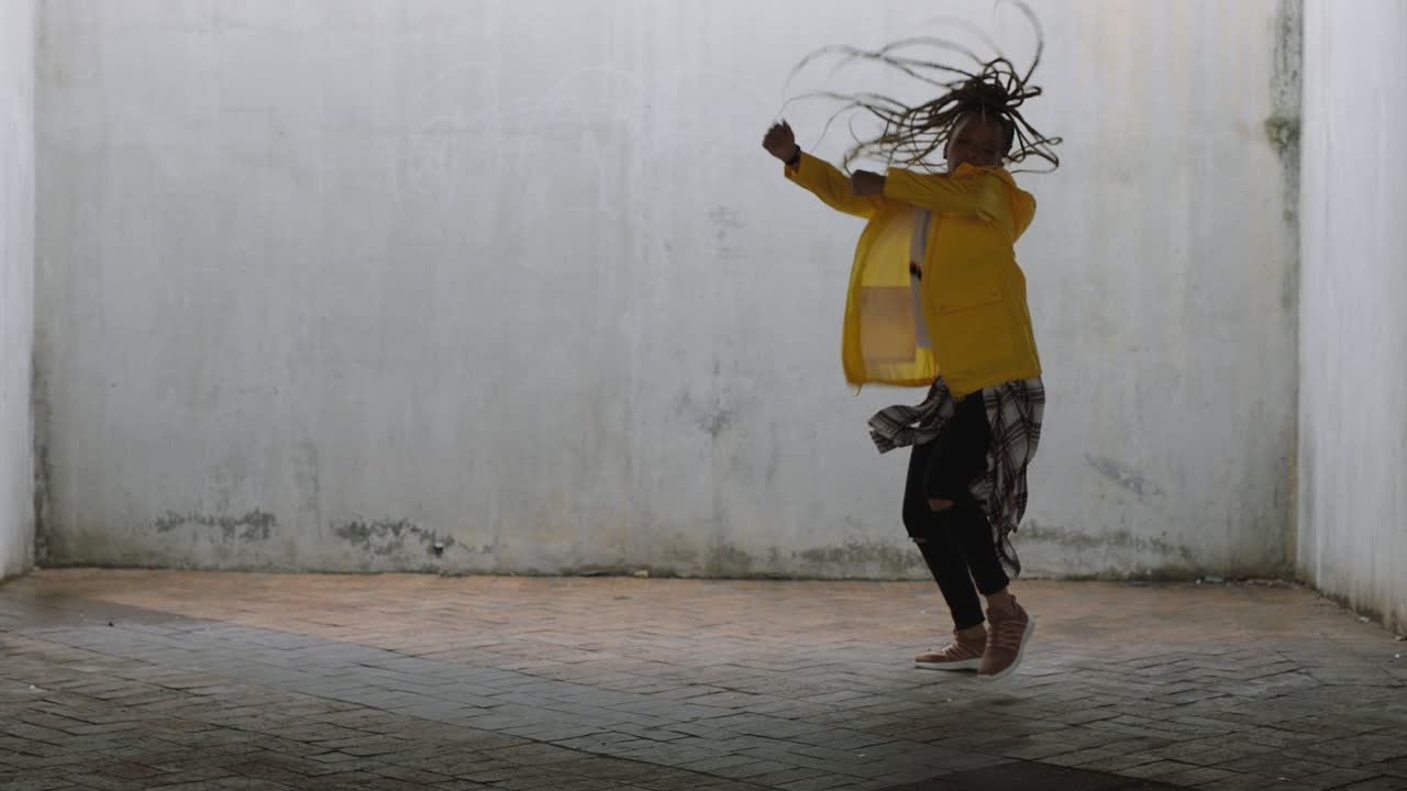 mujer bailarina joven bailarina de calle de raza mixta realizando movimientos de hip hop de estilo libre disfrutando de la expresión de danza moderna practicando en un almacén grungy con chaqueta amarilla