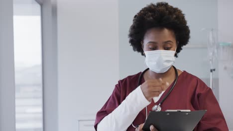 Portrait-of-happy-african-american-female-doctor-with-face-mask-in-hospital-room,-slow-motion