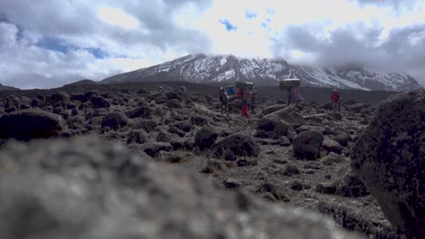 static shot of people carrying luggage on their heads, walking slowly, with mt kilimanjaro in the background